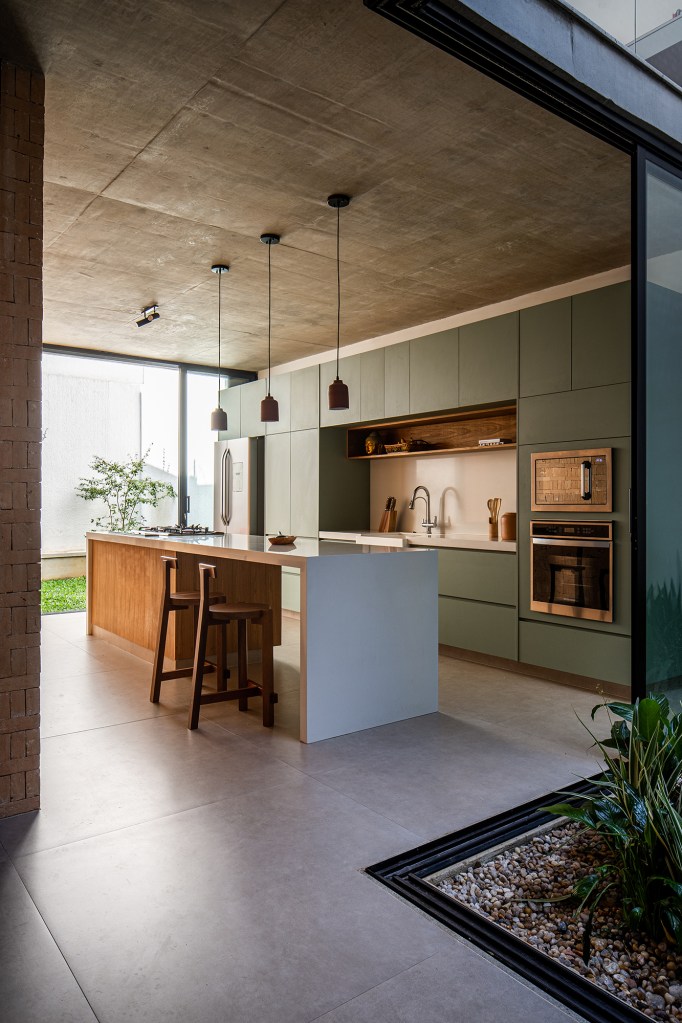 Átrio central e fachada vazada de tijolos marcam projeto de casa de 220 m². Projeto Eixo Arquitetos. Na foto, cozinha com bancada central e armários verdes.