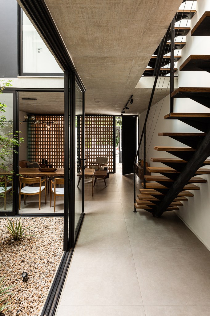 Átrio central e fachada vazada de tijolos marcam projeto de casa de 220 m². Projeto Eixo Arquitetos. Na foto, sala de jantar com jardim interno, escada e cozinha.