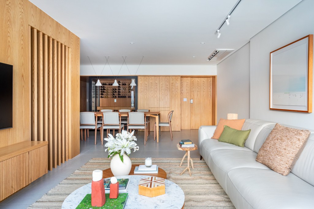 Projeto de Beta Arquitetura. Na foto, sala de estar integrada com jantar com sofá cinza claro e mesa de centro redonda.