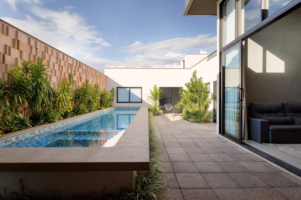 Borda de piscina elevada vira banco nesta casa comtemporânea de 209 m². Projeto de Leogigioli Arquitetos. Na foto, jardim com piscina elevada e sala integrada.