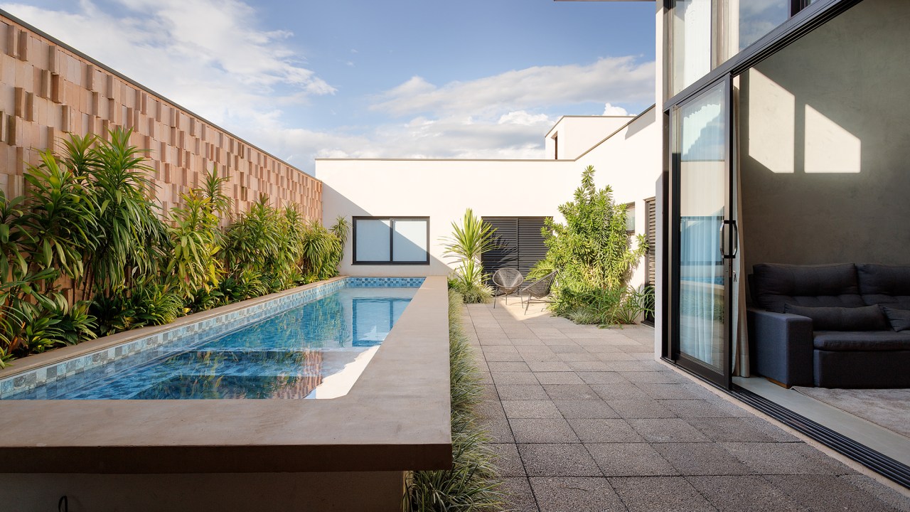 Borda de piscina elevada vira banco nesta casa comtemporânea de 209 m². Projeto de Leogigioli Arquitetos. Na foto, jardim com piscina elevada e sala integrada.