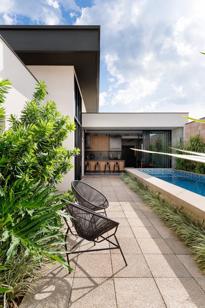 Borda de piscina elevada vira banco nesta casa comtemporânea de 209 m². Projeto de Leogigioli Arquitetos. Na foto, jardim com piscina elevada e cozinha integrada.