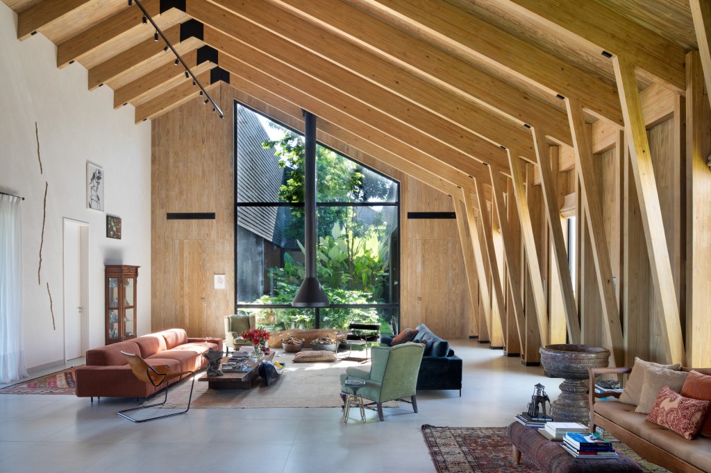 Casa celeiro de madeira une o rústico e o moderno em projeto de 1230 m². Projeto de Otto Felix. Na foto, sala de estar com paredes de madeira, lareira e vista para o jardim.