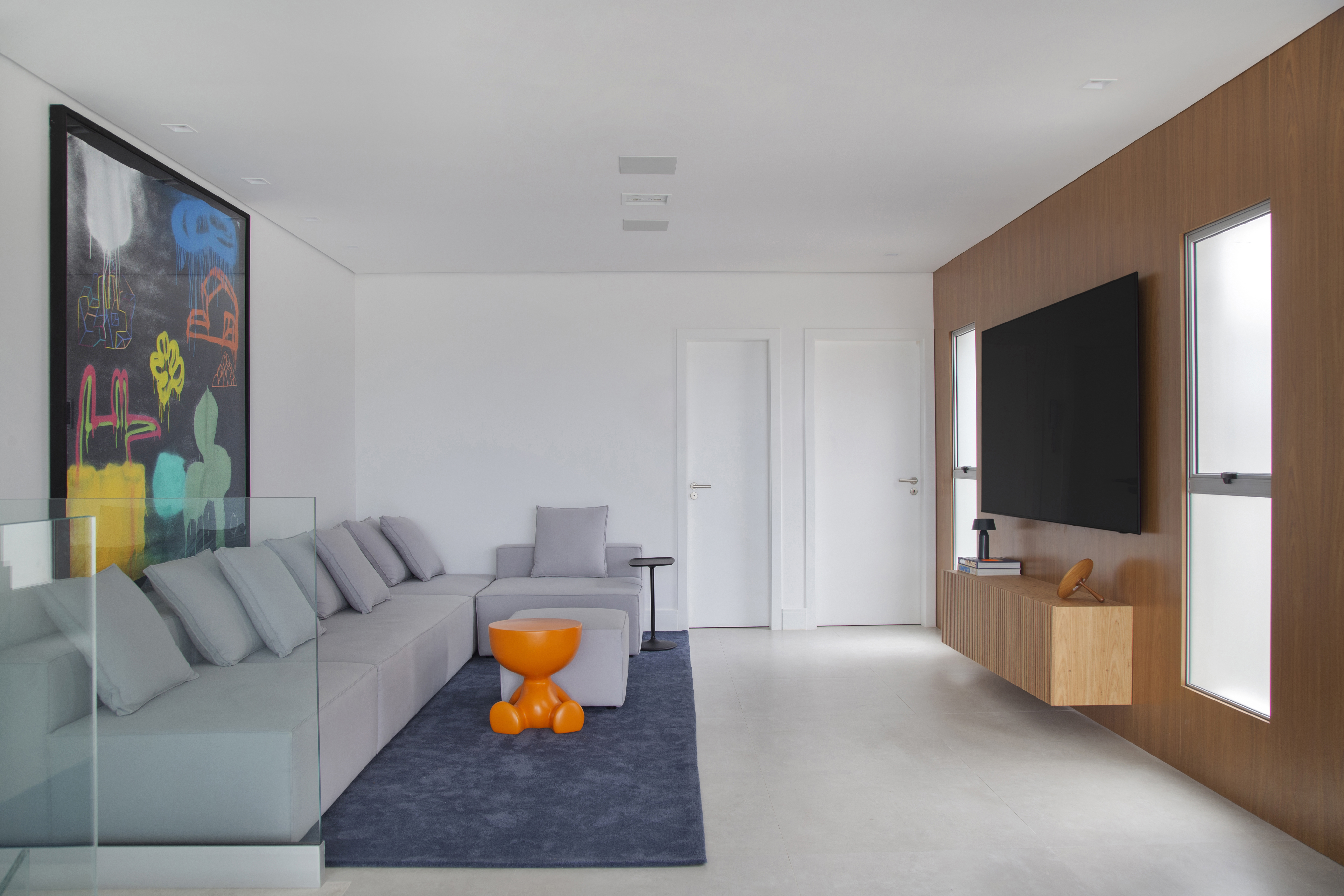Cobertura de 400m² para irmãos gêmeos tem closet espaçoso de 32m². Projeto de Tom Castro. Na foto, sala com sofá cinza, tapete azul e tv.