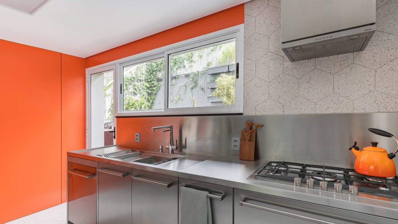 Cozinha ganha projeto moderno com acabamentos em inox e fórmica laranja. Projeto de Bia Hajnal.