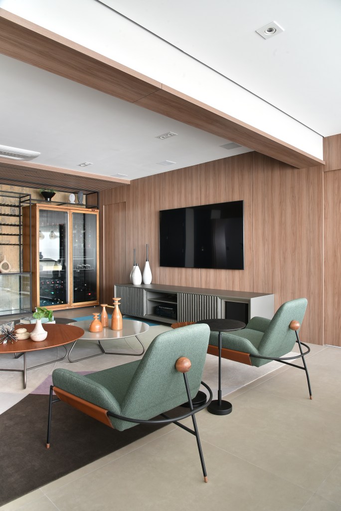 Decoração de apê de 149m² traz conforto pelos materiais naturais. Projeto de Rosangela Pena. Na foto, sala de estar com poltrona verde e parede revestida de madeira.