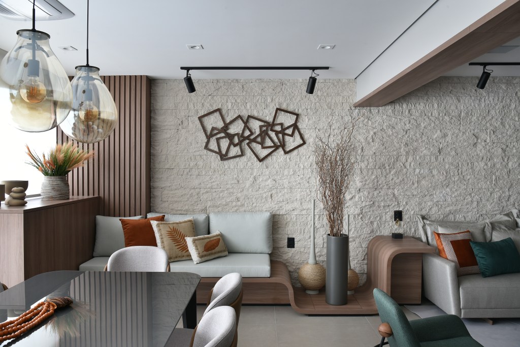 Decoração de apê de 149m² traz conforto pelos materiais naturais. Projeto de Rosangela Pena. Na foto, sala de estar com sofá claro e parede de pedras.