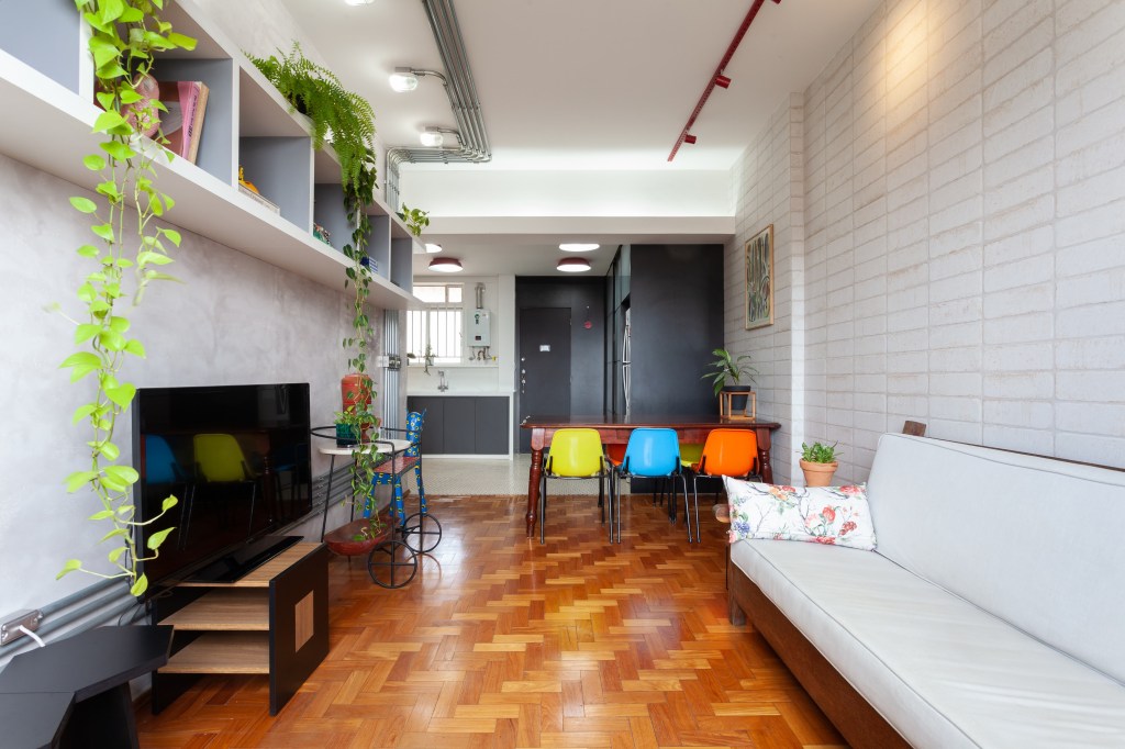 Estilo industrial e móveis retrô marcam apê de 75 m² em Belo Horizonte. Projeto de Mutabile Arquitetura. Na foto, sala com piso de madeira, cadeiras coloridas e cimento queimado.