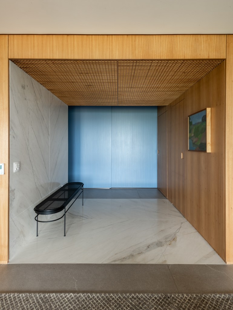 Forro iluminado de muxarabi cria sensação de luz natural em apê de 278 m². Projeto de Cris Furlan. Na foto, sala de estar com parede de madeira. Parece ripada azul.
