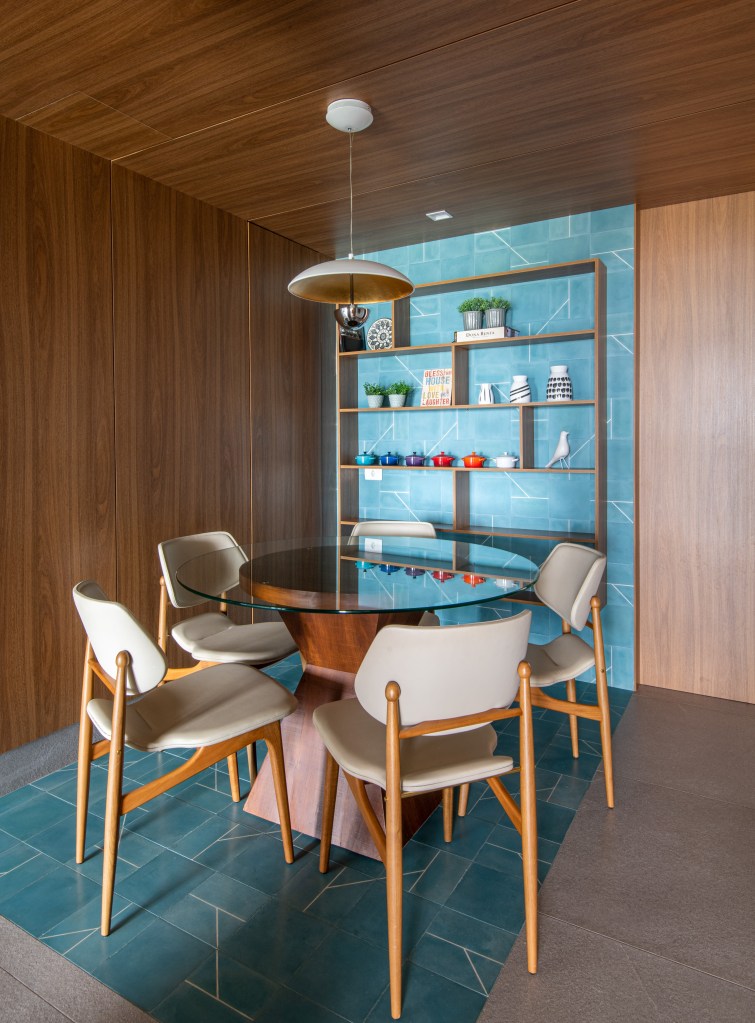 Forro iluminado de muxarabi cria sensação de luz natural em apê de 278 m². Projeto de Cris Furlan. Na foto, sala de almoço com mesa de vidro e piso e parede azuis.