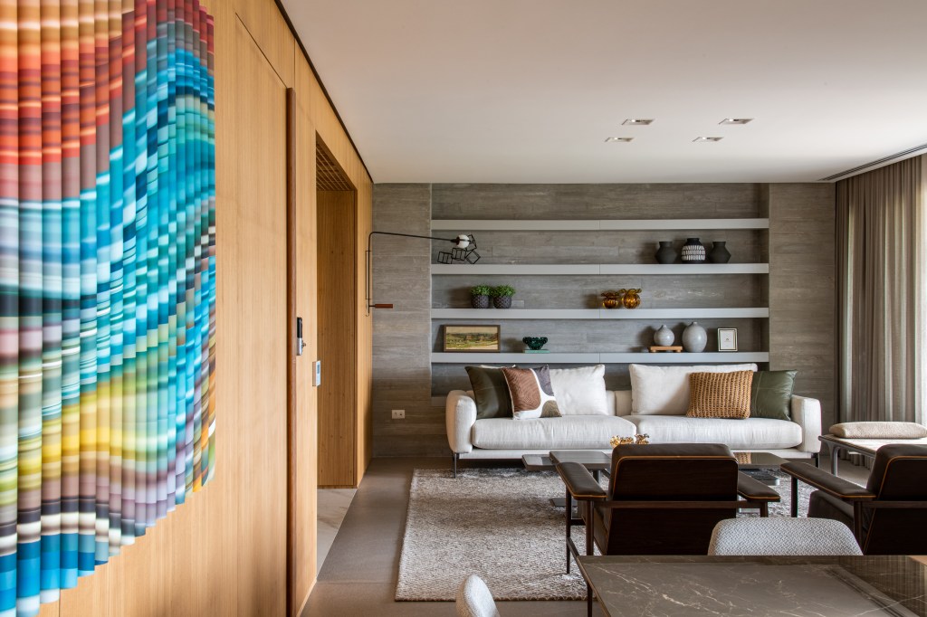 Forro iluminado de muxarabi cria sensação de luz natural em apê de 278 m². Projeto de Cris Furlan. Na foto, sala de estar com estante embutida e parede de madeira.