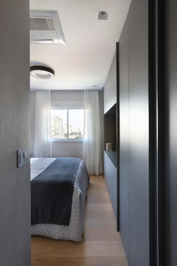 5 jeitos que a marcenaria planejada ajuda em quartos pequenos com exemplos. Projeto de Fernando Mota. Na foto, quarto com marcenaria escura.