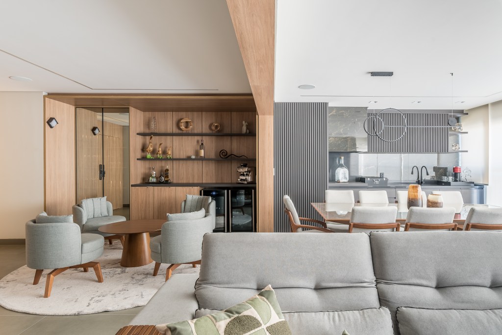 Marcenaria e sofá de 4m são destaques em apê aconchegante de 159m². Projeto de Elvira Oliveira Arquitetura. Na foto, sala de estar integrada com sofá cinza e adega.