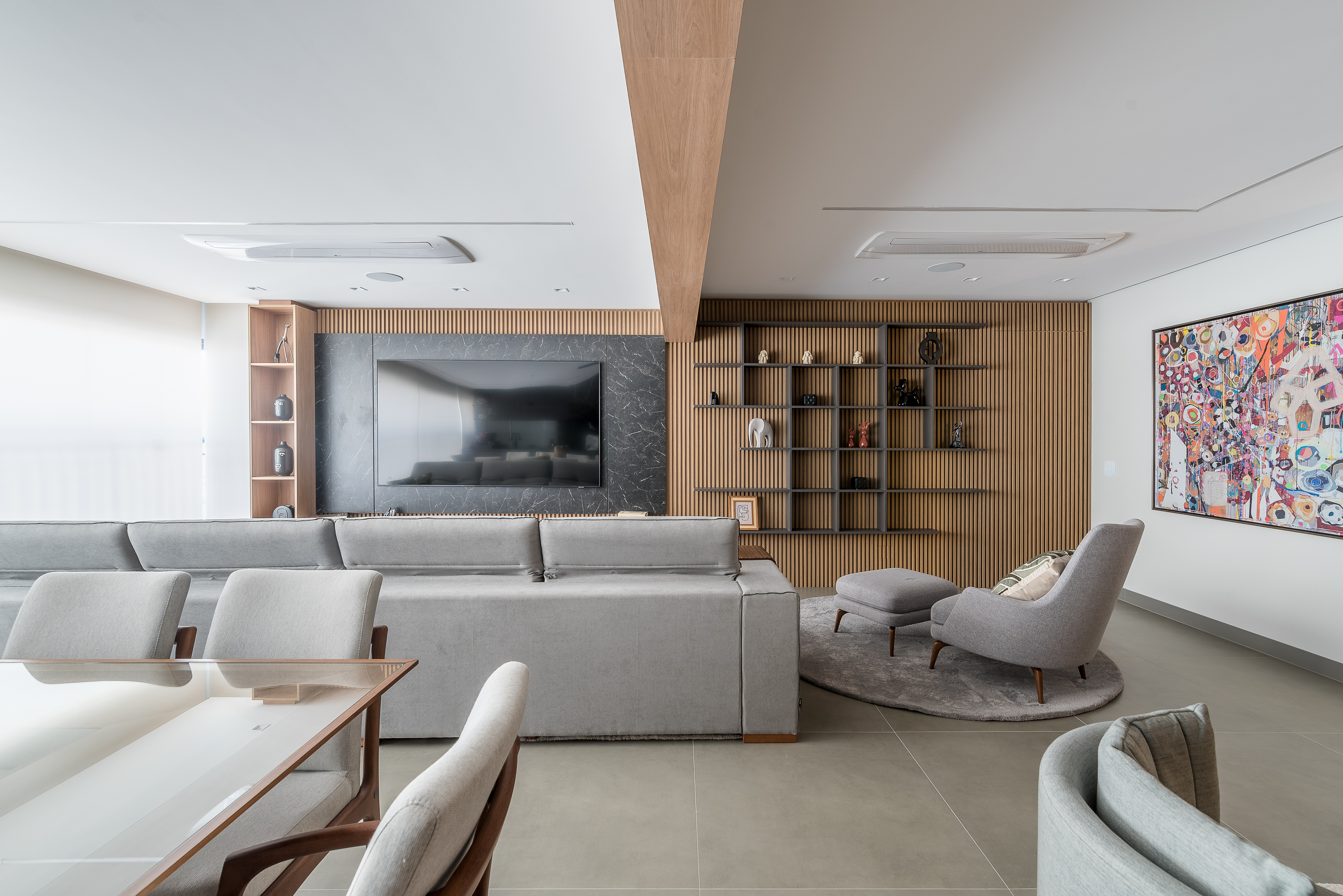 Marcenaria e sofá de 4m são destaques em apê aconchegante de 159m². Projeto de Elvira Oliveira Arquitetura. Na foto, sala de estar com sofá cinza, painel marmorizado e parede ripada.