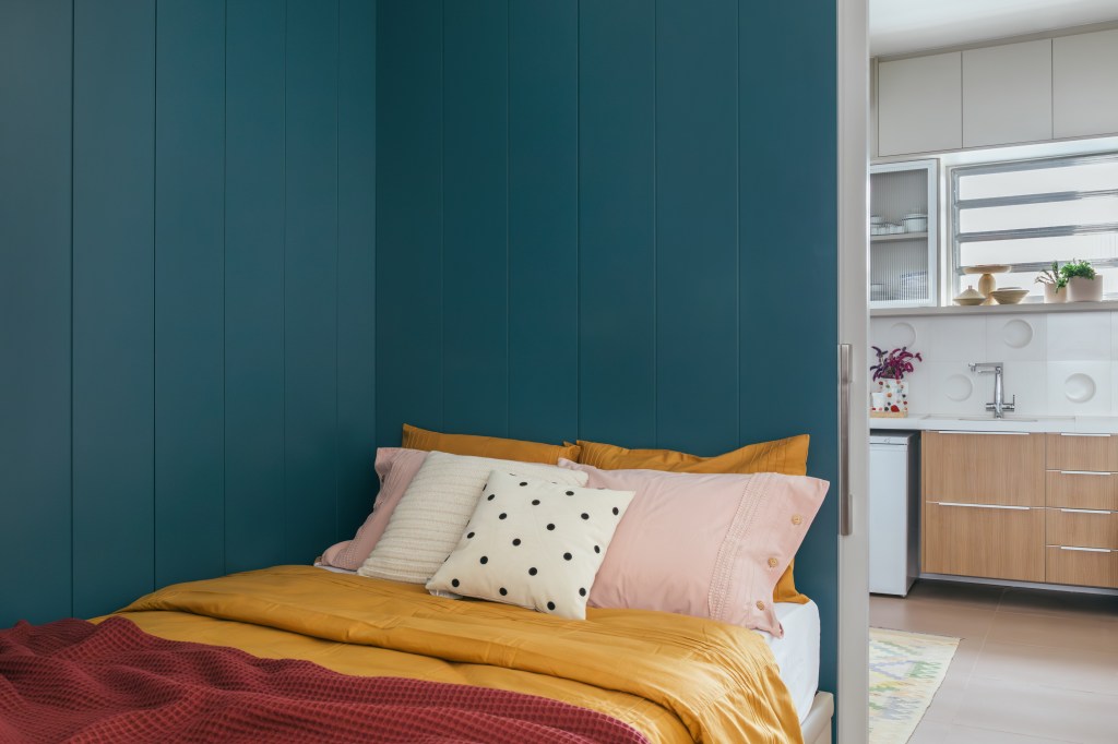 Projeto de Casa Cururu Arquitetura. Na foto, quarto com parede azul e roupa de cama vermelha e amarela.