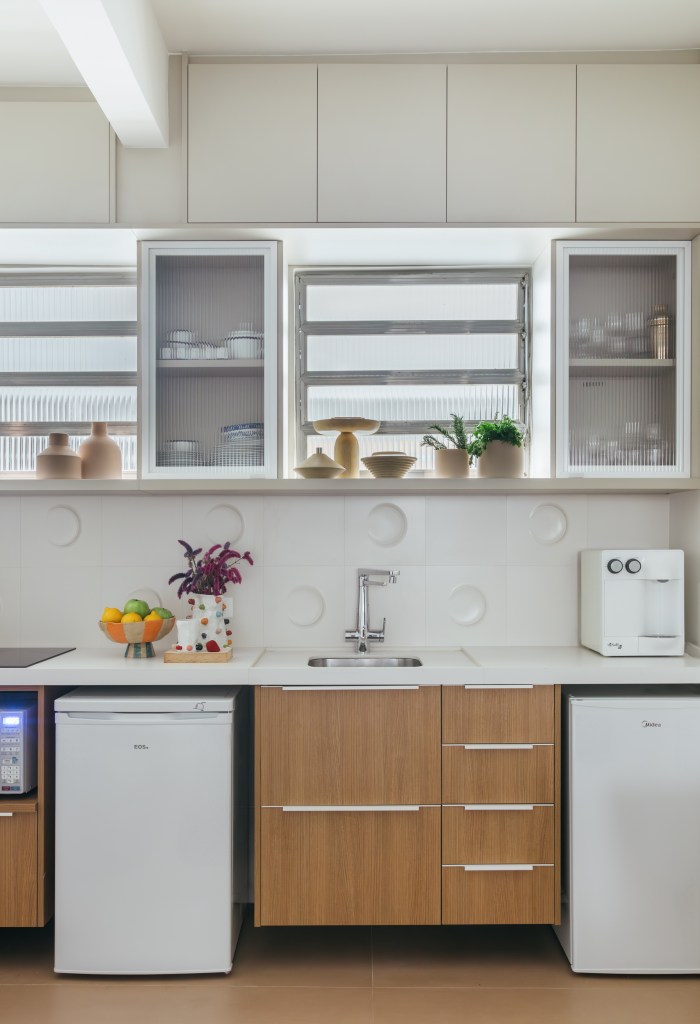 Projeto de Casa Cururu Arquitetura. Na foto, cozinha pequena com bancada branca, frigobar e armários brancos com portas de vidro.