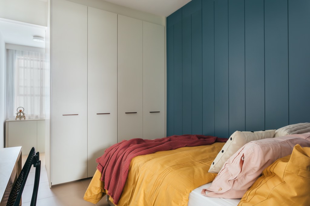 Projeto de Casa Cururu Arquitetura. Na foto, quarto com parede azul, armário branco e roupa de cama vermelha e amarela.