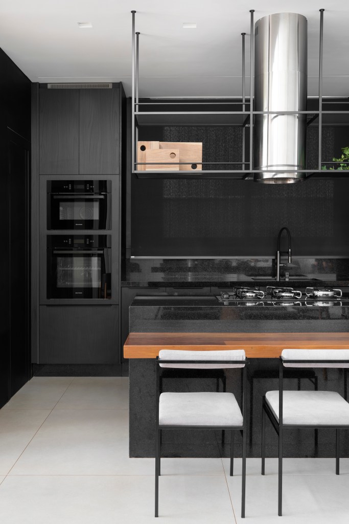 Minimalismo e décor contemporâneo marcam casa térrea de 273m². Projeto de Piacesi Arquitetos. Na foto, cozinha com mesa de madeira e marcenaria preta.