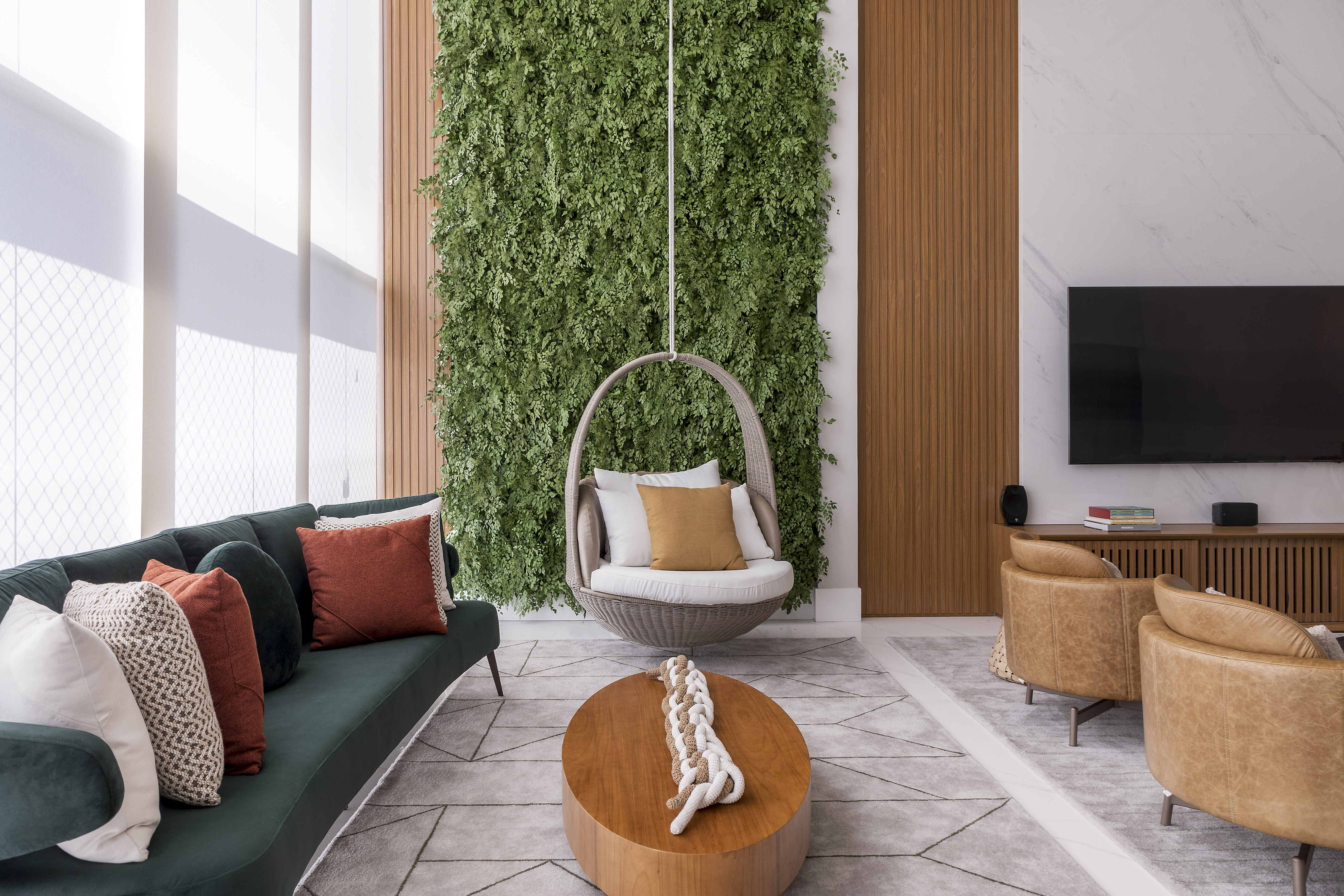 Painel ripado e marmorizado em pé-direito duplo é destaque em apê de 240m². Projeto de Marta Martins. Na foto, sala com pé-direito duplo, jardim vertical, balanço e sofá verde.
