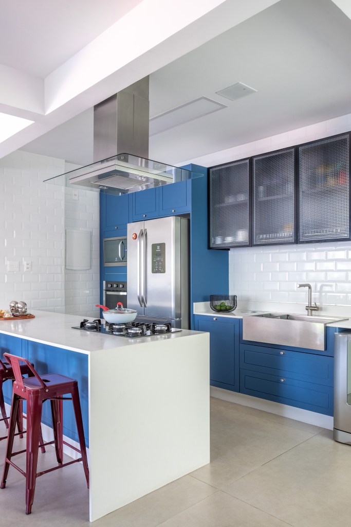 Papel de parede floral e toques de azul dão ar cozy à este apê de 200m². Projeto de Ana Cano. Na foto, cozinha com marcenaria azul e bancada branca.