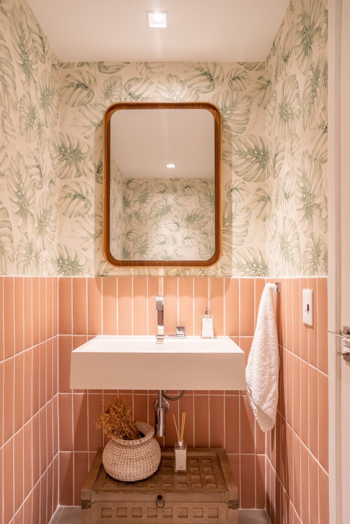 Papel de parede floral e toques de azul dão ar cozy à este apê de 200m². Projeto de Ana Cano. Na foto, lavabo com meia parede de azulejo rosa e papel de parede.