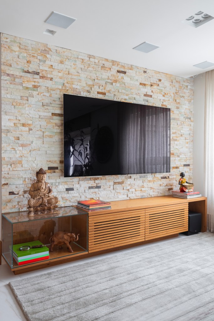 Projeto de Tatu Arquitetura. Na foto, sala de tv com parede de tijolinhos e sofá cinza.