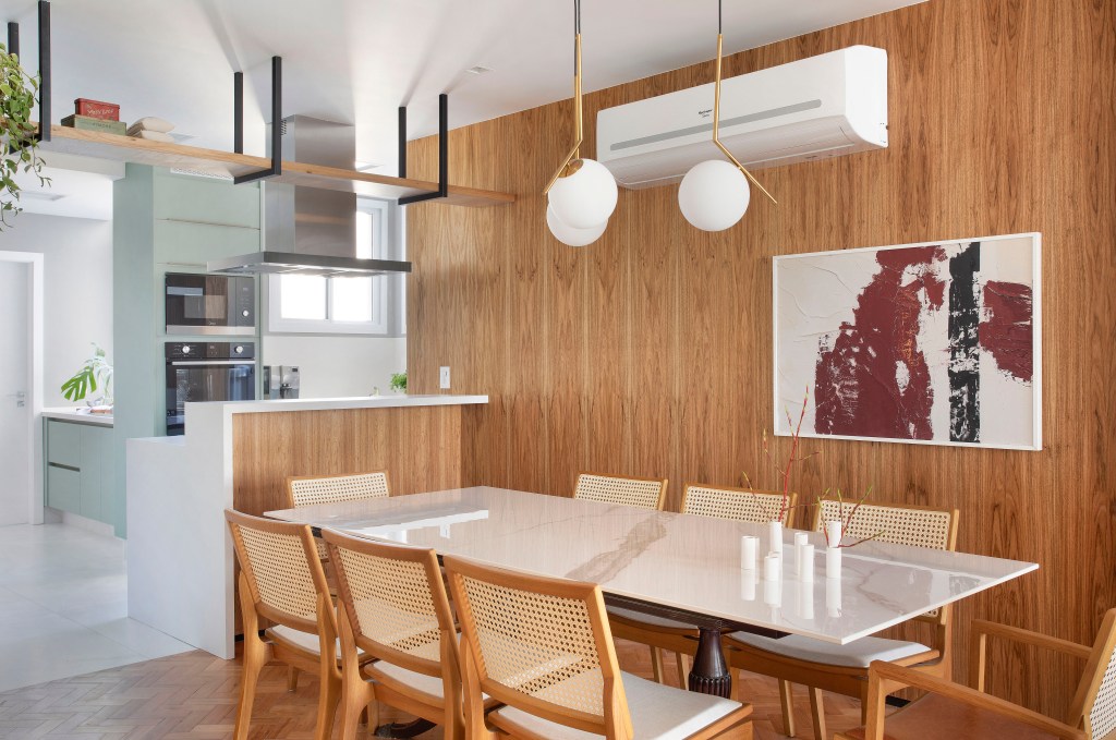 Projeto de Henrique Ramalho. Na foto, sala de jantar com mesa de tampo branco, cadeira com encosto de palhinha e cozinha integrada.