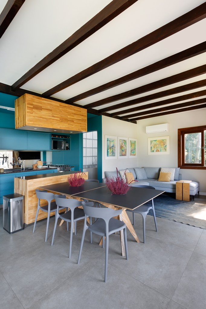Reforma em casa dos anos 1960 ganha projeto sustentável e saunas no jardim. Projeto de Bia Hajnal. Na foto, sala de estar com lareira e sofá em L. Cozinha com ilha e parede verde.