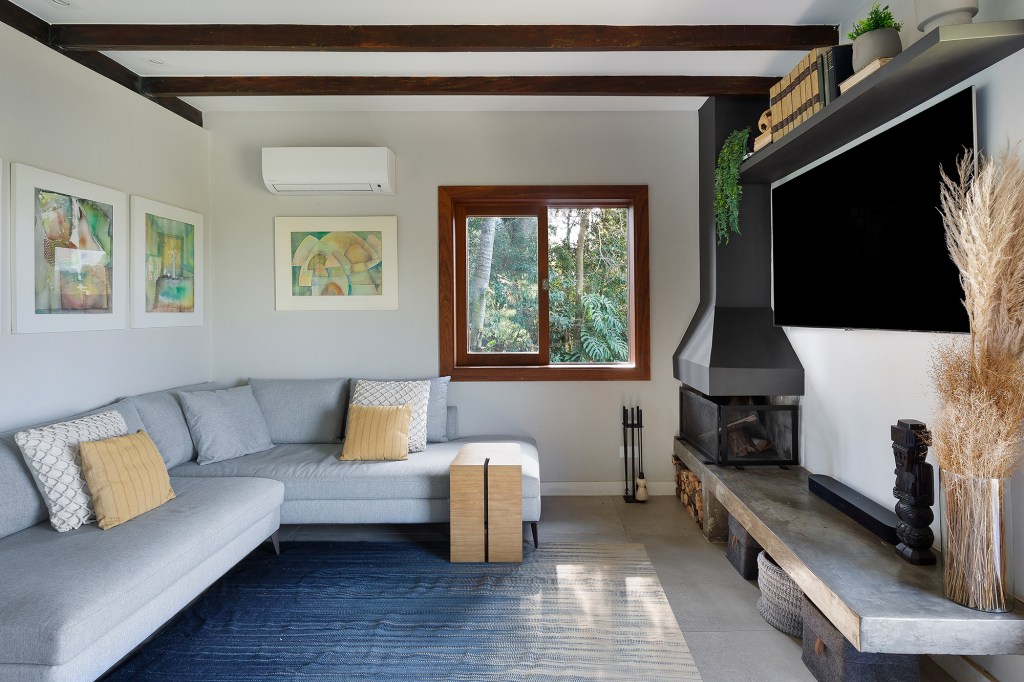 Reforma em casa dos anos 1960 ganha projeto sustentável e saunas no jardim. Projeto de Bia Hajnal. Na foto, sala de estar com lareira e sofá em L.