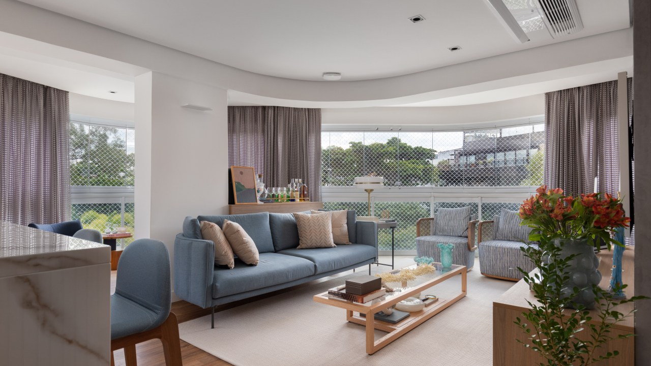 Projeto de CC5 arquitetura e interiores. Na foto, sala de estar com layout curvo, sofá azul e tapete bege.