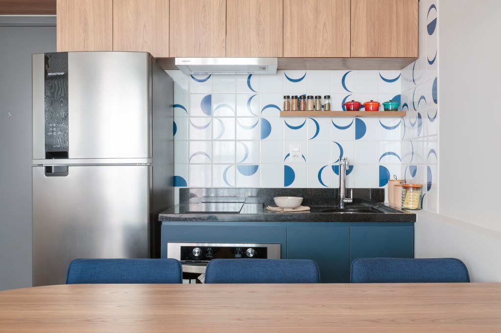 Projeto de Estúdio Maré. Na foto, cozinha integrada com parede de azulejos e bancada com cadeiras azuis. Marcenaria azul.