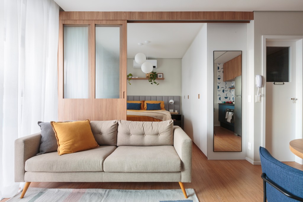 Projeto de Estúdio Maré. Na foto, sala de estar com sofá cinza e porta de correr para quarto.