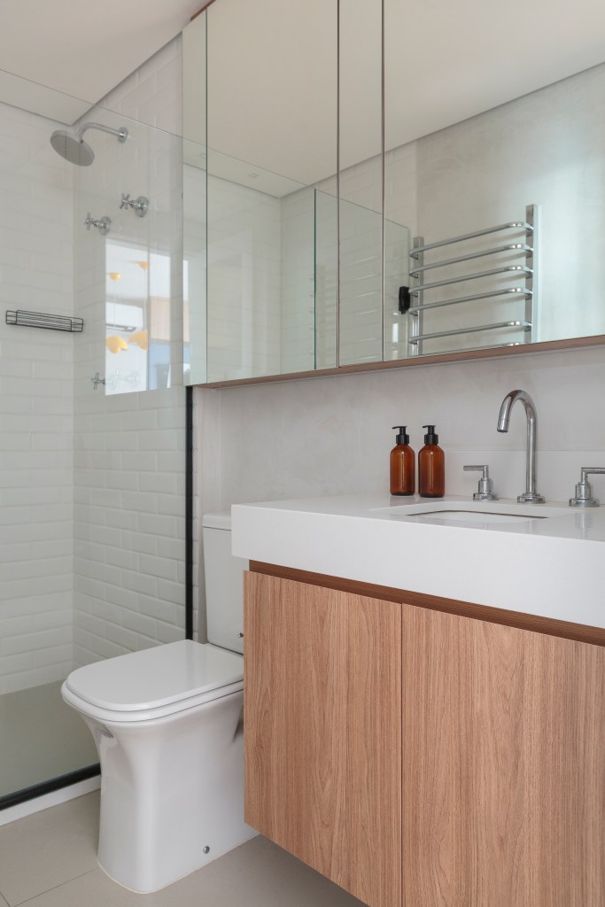 Projeto de Estúdio Maré. Na foto, banheiro com bancada branca e armário espelhado iluminado.