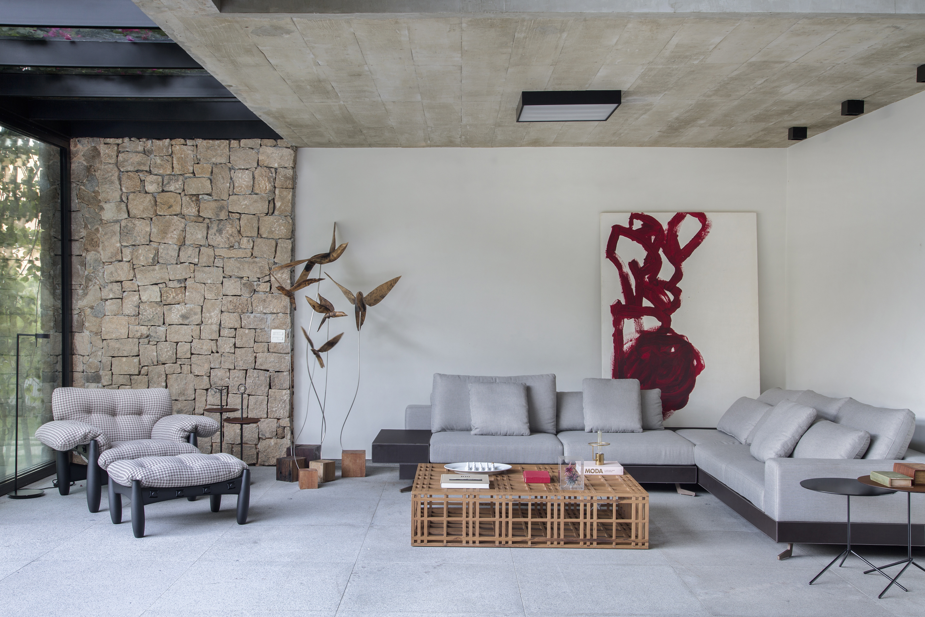 A varanda desta residência de 511 m² fica dentro de casa. Projeto Sabugosa Arquitetura. Sala de estar integrada ao jardim com parede de pedra, poltrona mole e sofá em l.