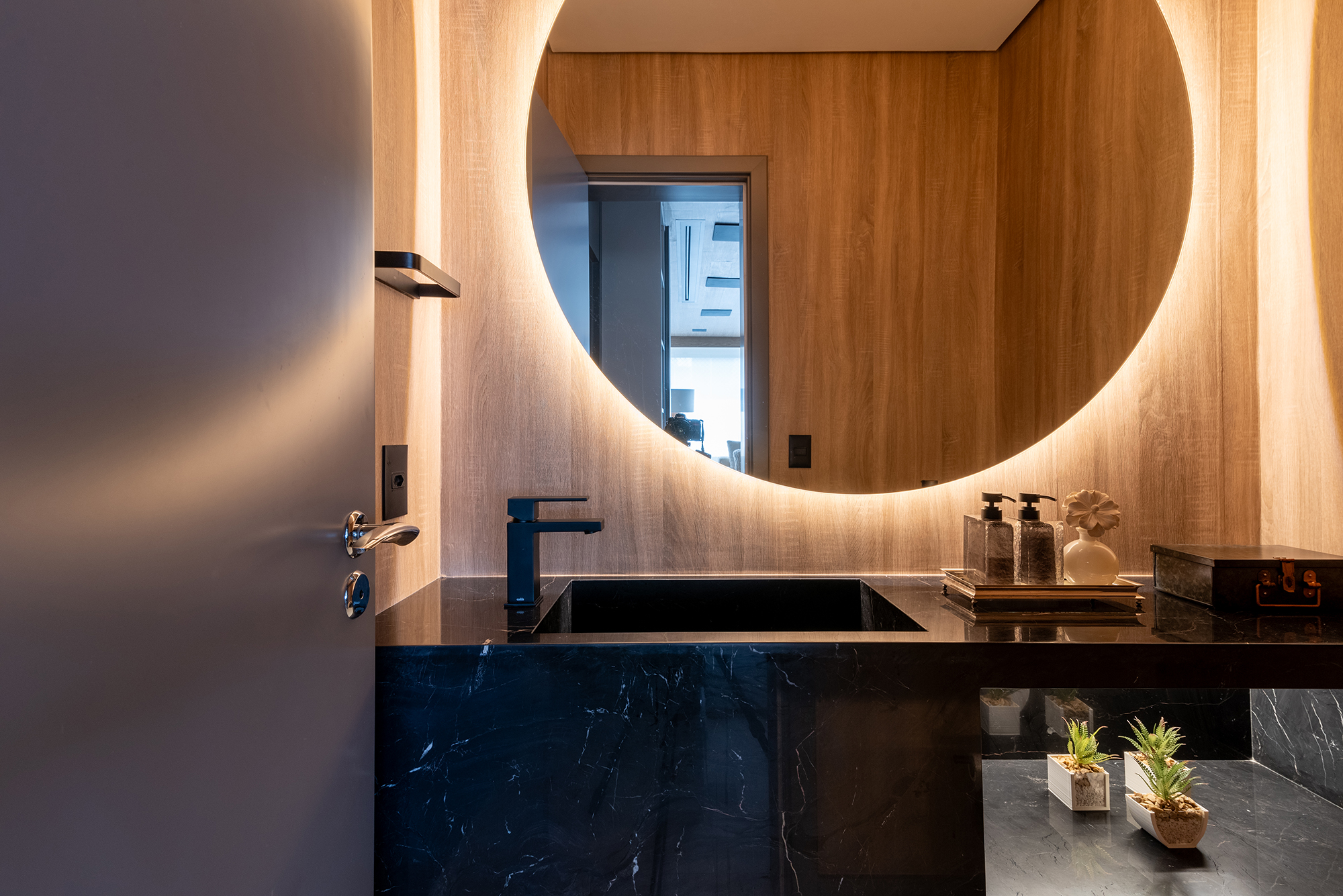 Apê de 211 m² com vista para Ponte Estaiada mescla pedras nobres no décor. Projeto de Juliana Sica. Na foto, lavabo com espelho redondo iluminado.