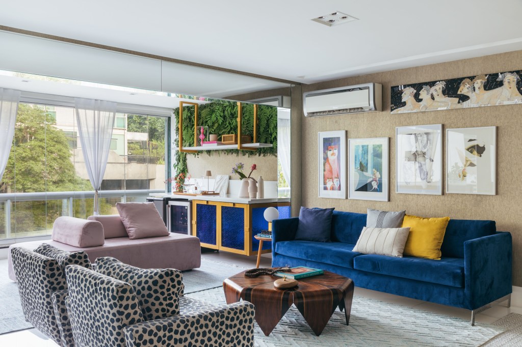 Apê de Ciro Bottini tem paleta Art Deco Navy com tons azuis e dourados. Projeto de Casa Cururu. Na foto, sala integrada com varanda com sofá azul, rosa e poltrona com estampa animal.