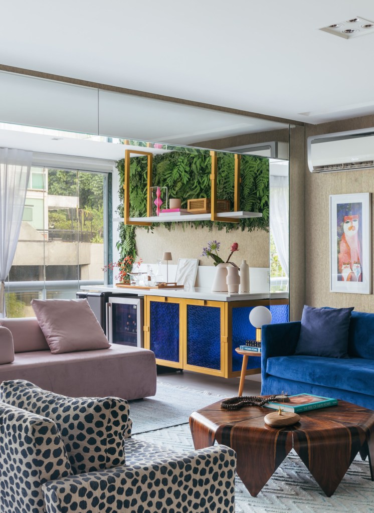 Apê de Ciro Bottini tem paleta Art Deco Navy com tons azuis e dourados. Projeto de Casa Cururu. Na foto, sala integrada com varanda com sofá azul, rosa e poltrona com estampa animal.