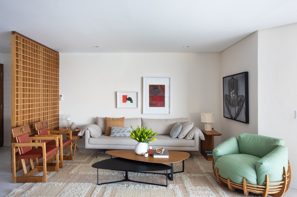 Apê de 270m² ganha piso de porcelanato marmorizado e sala íntima. Projeto de Henrique Ramalho. Na foto, sala de estar com tapete neutro, sofá cinza e poltrona verde.