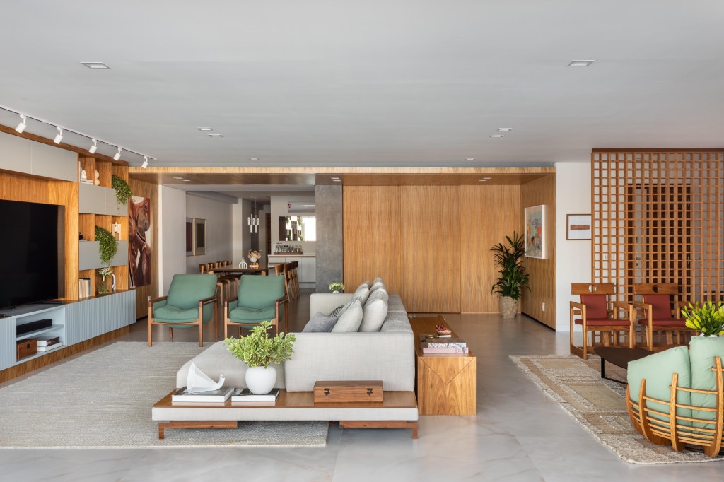 Apê de 270m² ganha piso de porcelanato marmorizado e sala íntima. Projeto de Henrique Ramalho. Na foto, sala integrada com piso de porcelanato, porta de correr de madeira e sofá cinza.
