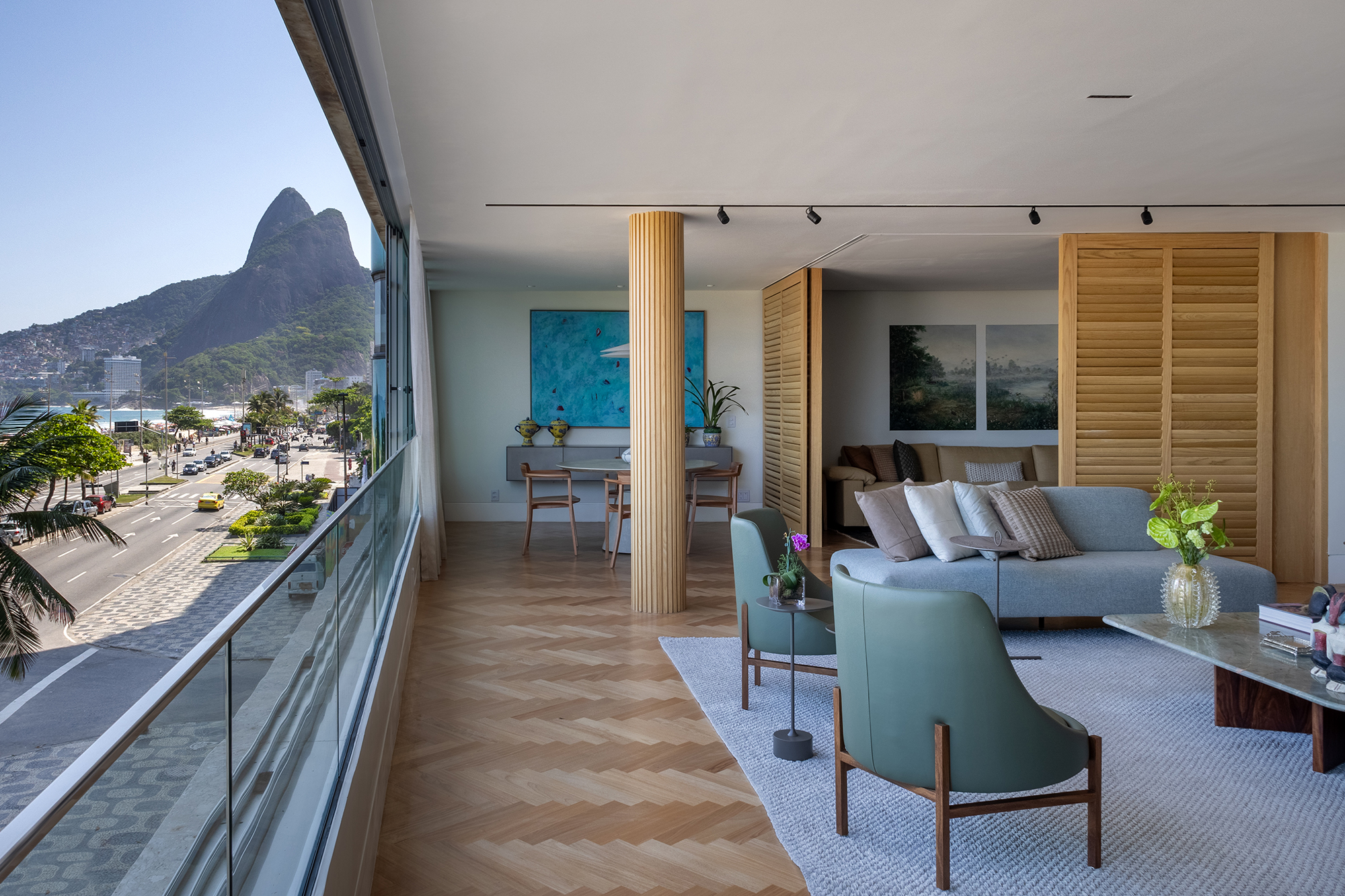 Apê de 300 m² tem vista para o mar e duas mesas iguais de jantar. Projeto de Andrea Chicharo. Na foto, sala de estar com brise, sofás e vista para o mar.