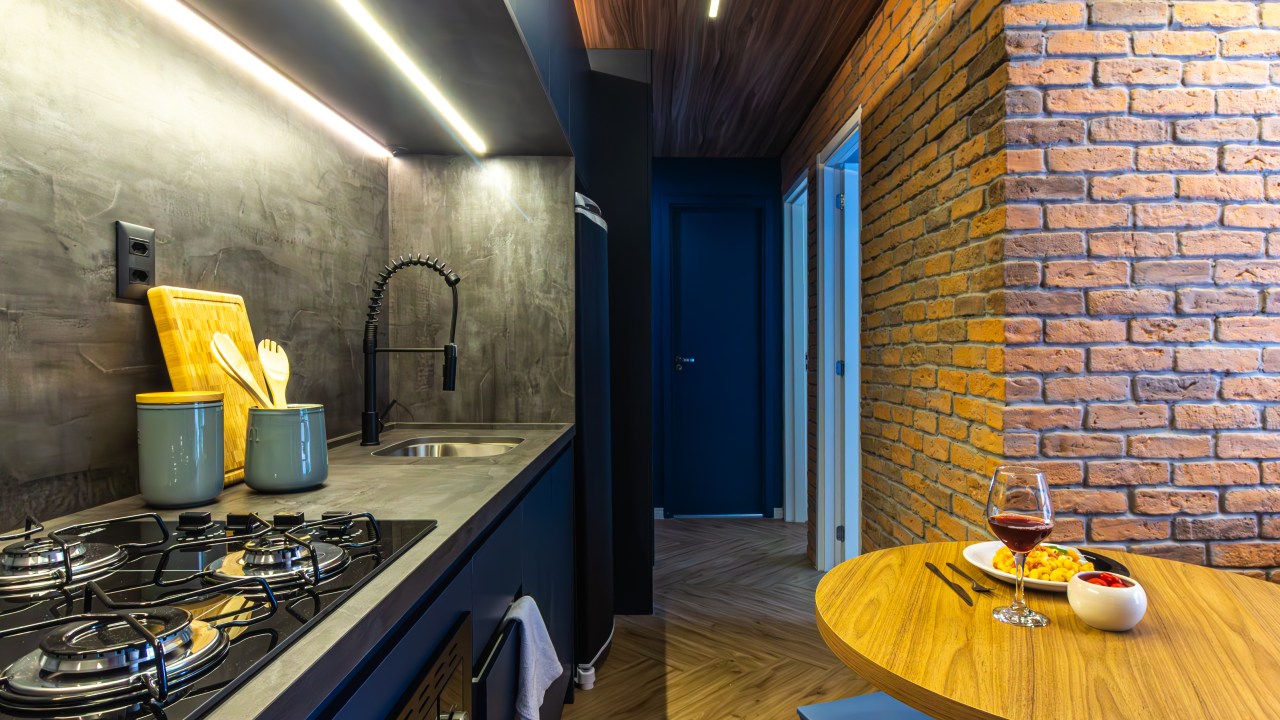 Apê de 39 m² tem cozinha azul, tijolos rústicos e quarto de hóspedes. Projeto de Larice Sena. Na foto, cozinha com marcenaria azul e parede de tijolos rústicos.