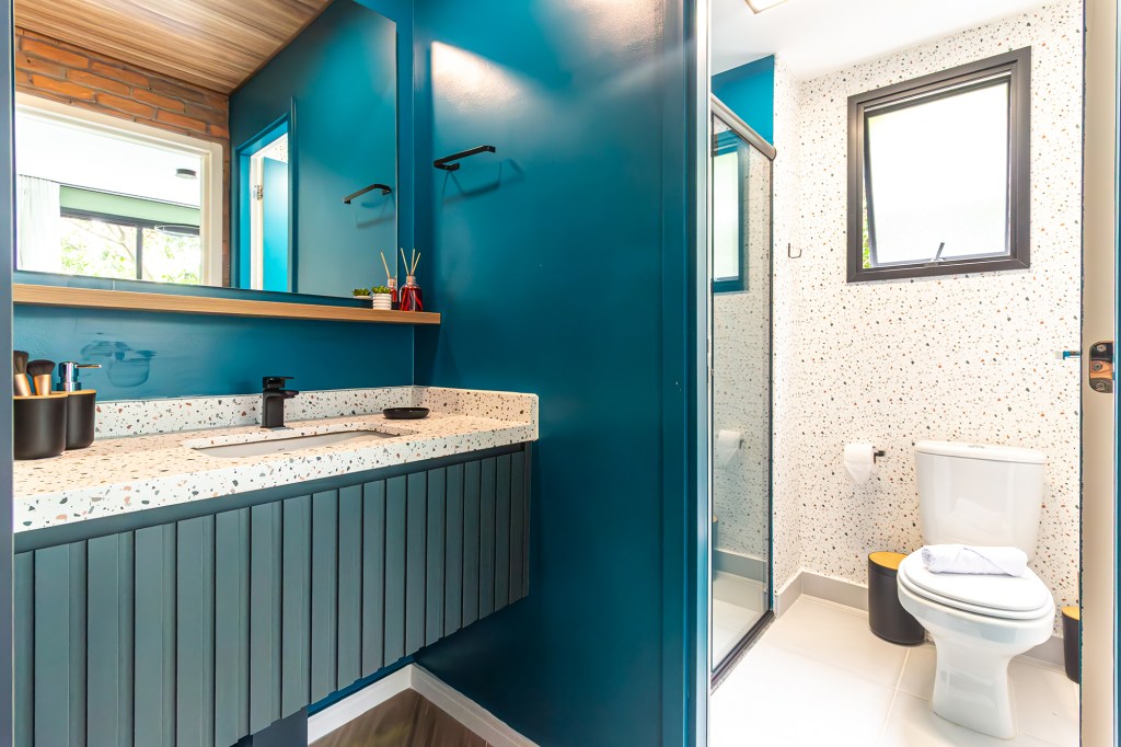 Apê de 39 m² tem cozinha azul, tijolos rústicos e quarto de hóspedes. Projeto de Larice Sena. Na foto, banheiro com granilite, parede colorida e espelho.