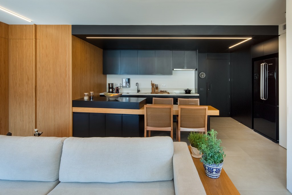 Apê de 90 m² tem cozinha com marcenaria preta e cuba triangular no lavabo. Projeto de Joaquim Meyer. Na foto, cozinha com marcenaria preta integrada com a sala de estar.