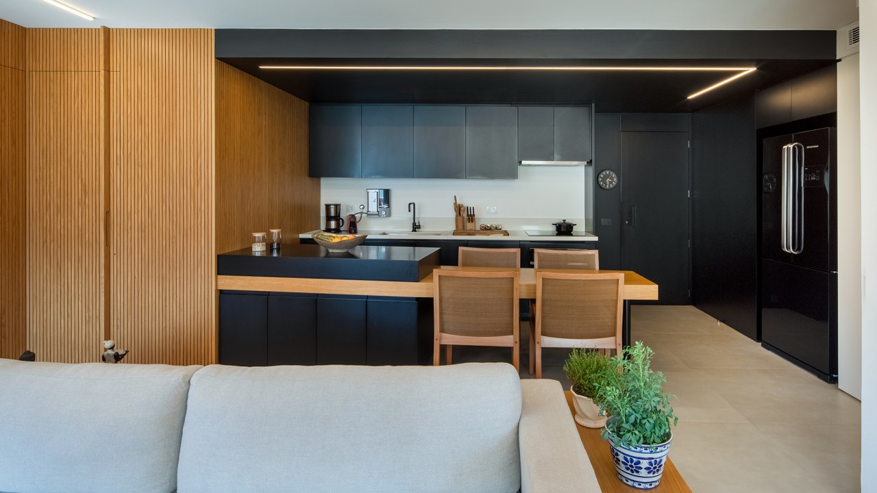 Apê de 90 m² tem cozinha com marcenaria preta e cuba triangular no lavabo. Projeto de Joaquim Meyer. Na foto, cozinha com marcenaria preta integrada com a sala de estar.
