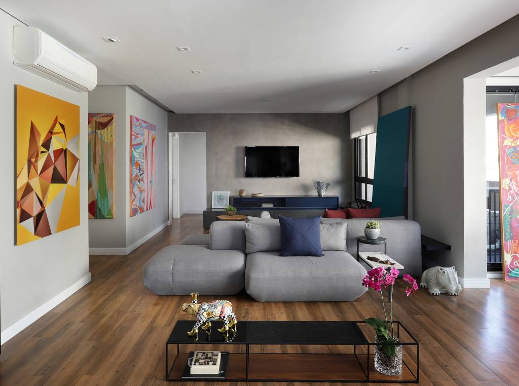 Apê descolado de 120 m² tem décor inspirado nos quadros do cliente. Projeto Inovando Arquitetura. Na foto, sala com sofá ilha cinza, quadros e parede de cimento queimado.