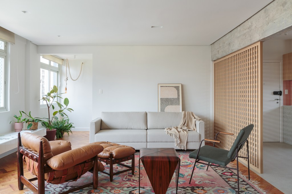 Banco com azulejos estampados e espaço pet são destaques no apê de 160 m². Projeto Estúdio Maré, Sala de estar com tapete. Parede muxarabi.