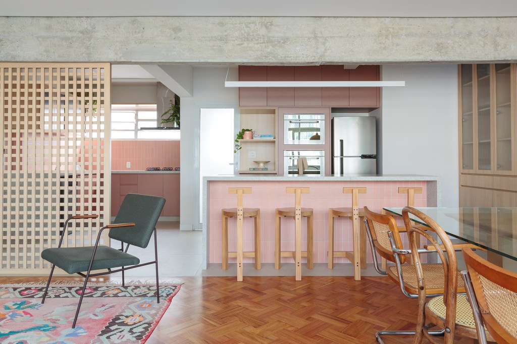 Banco com azulejos estampados e espaço pet são destaques no apê de 160 m². Projeto Estúdio Maré, Na foto, cozinha com ilha e revestimentos rosas. Parede de muxarabi.