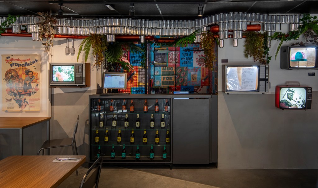 Bar em homenagem ao Mussum remete à vida e carreira do Trapalhão. Projeto de Superlimão. Na foto, bar com tvs e decoração de latas de cerveja.