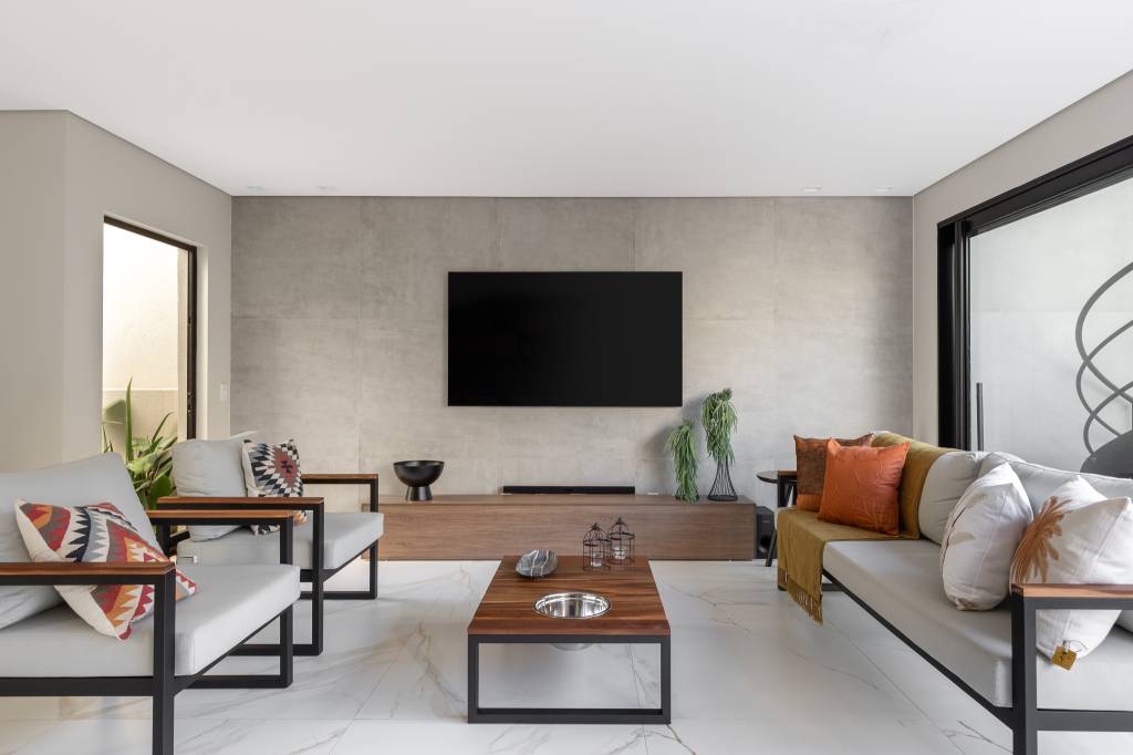 Casa com arquitetura clean foi pensada para as festas da família. Projeto de Visivo Arquitetura. Na foto, sala de TV com parede de cimento queimado e sofás.