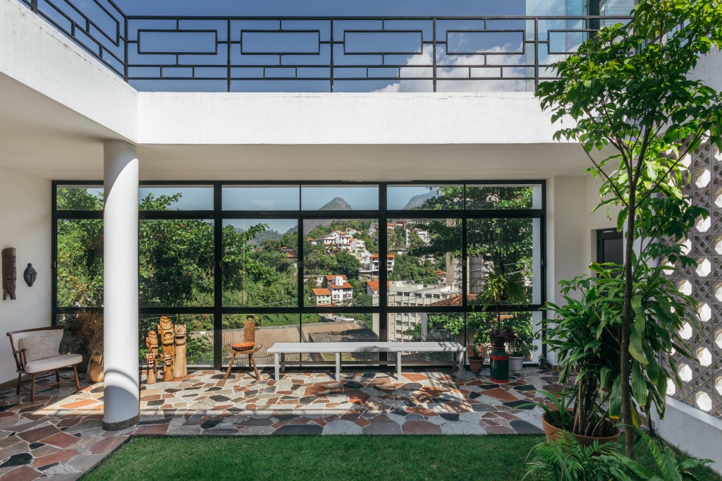 Casa de casal de 70 anos apaixonado por samba inspira-se na brasilidade. Projeto de Ana Cano. Na foto, área externa com piso de azulejo colorido e gramado.
